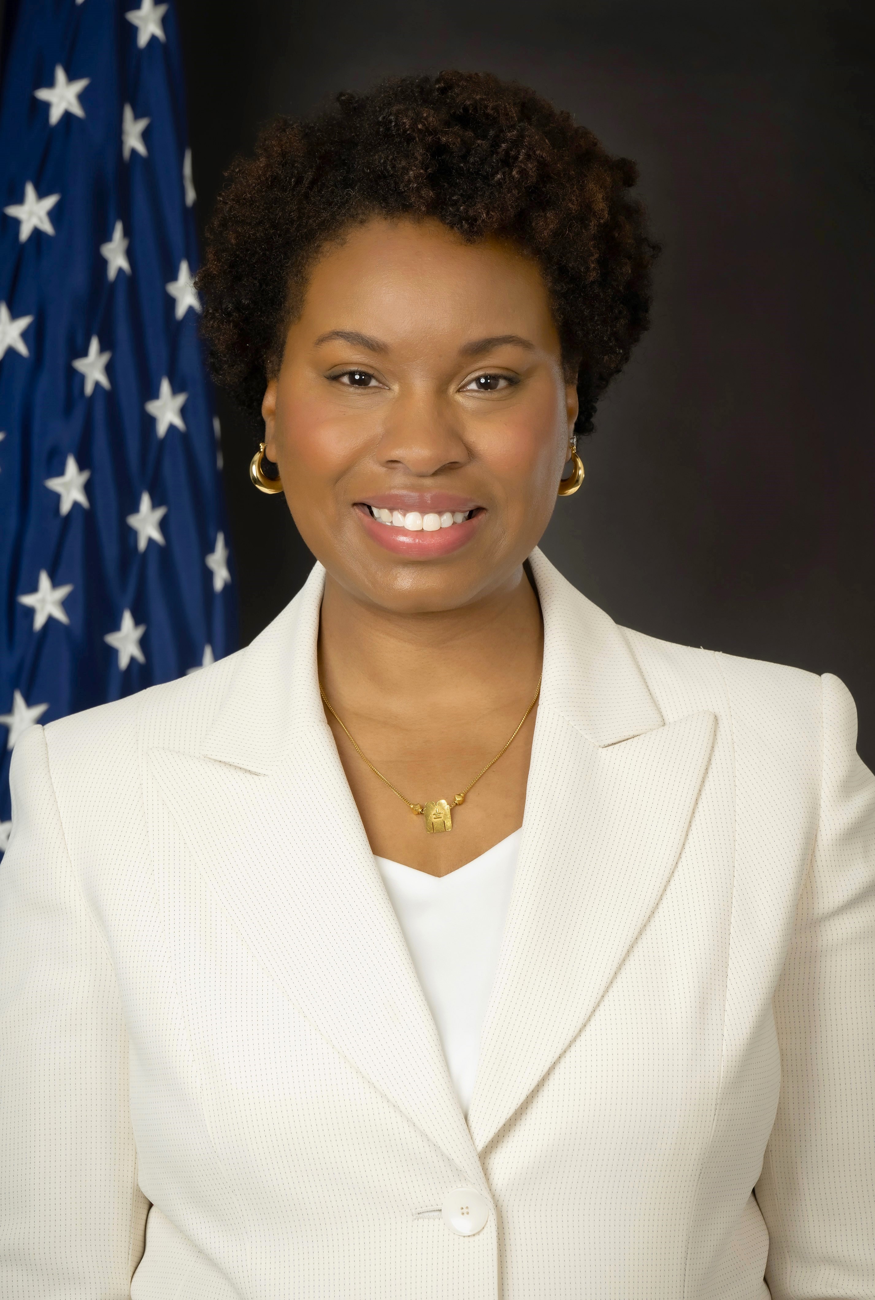 Black woman in white suit in front of American Flag