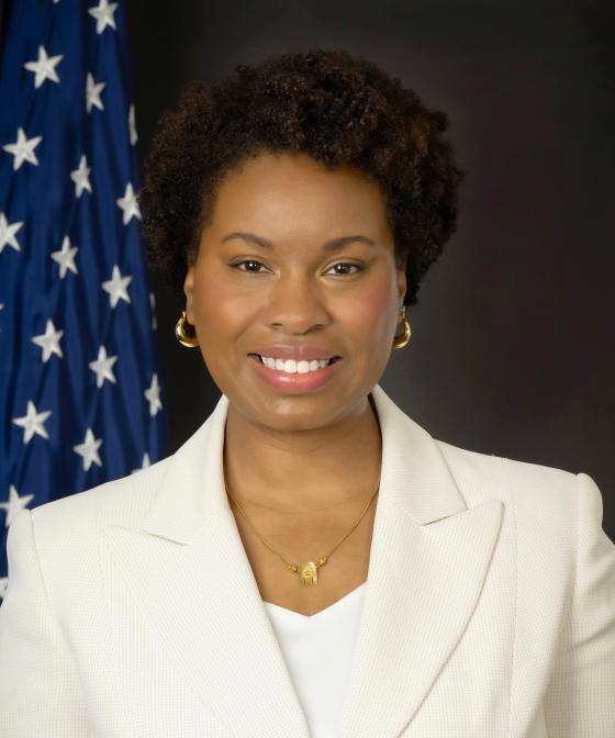 Black woman in white suit in front of American Flag